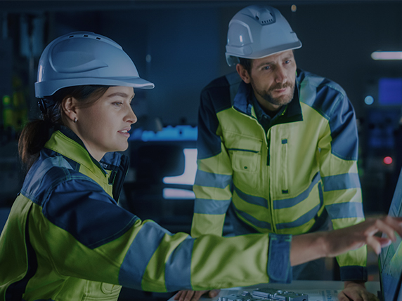 two people in hard hats looking at a computer