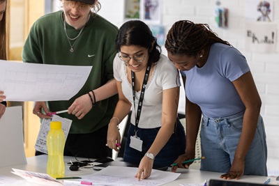 3 students working together, one of them holing a paper and another one pointing to some notes
