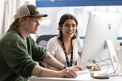 2 students, a female and a male working together at a computer smiling