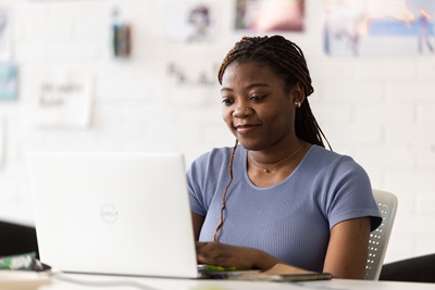 Female student wearing a blue top working on her computer and smiling