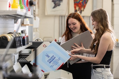 2 female students holding graphic design portfolio and smiling