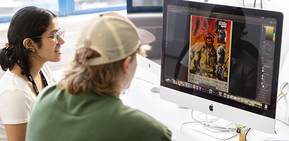 Two students sat at a Mac computer working on a graphic design project.