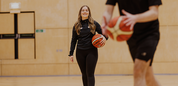 Student-athlete holding a basketball in Sport Central. She's looking directly at the camera and smiling.
