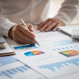Person using a pen adding notes to sheets of paper contained different graphs and charts 