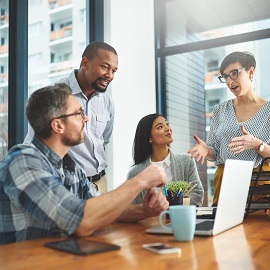 Four colleagues together in an office setting over a laptop and coffee having a discussion