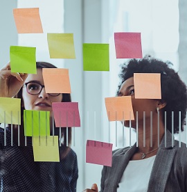 Colleagues reviewing different coloured post it notes laid out on  glass window 