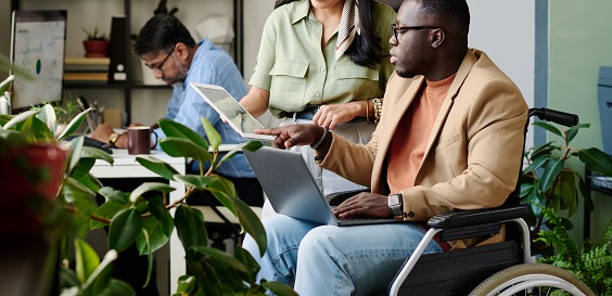 A person in a wheelchair using a computer talking to a colleague in an office