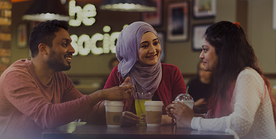 Three students gathered round a table, socialising. They're each holding a takeaway coffee cup.