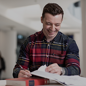 A student in a checkered shirt is laughing whilst taking notes
