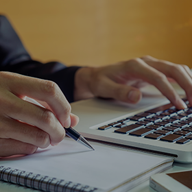 Close-up of a person taking notes and using their laptop