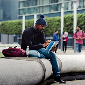 Student sat outside the Business Building, using an iPad.