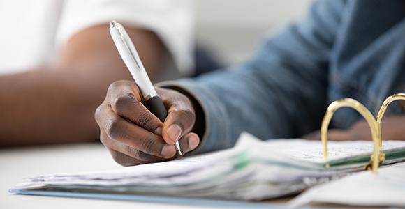 Close-up of an individual writing in a folder. They are holding a Northumbria-branded pen.