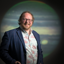 Professor Tom Stallard pictured in front of an image of Jupiter
