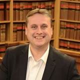a smiling man in a suit standing in front of a book shelf