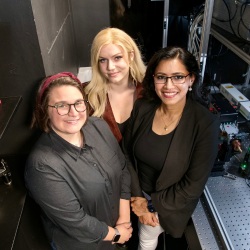 pictured are three women, standing side by side, in a lab with equipment around them.