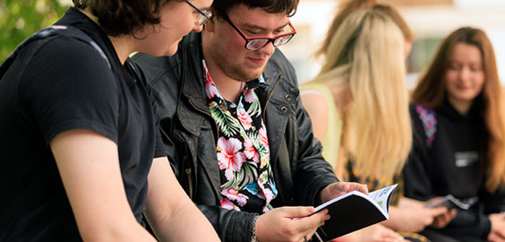 Two male student browsing a guidance booklet - female student chatting in the background