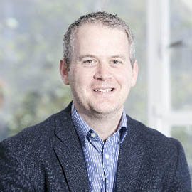 a man wearing a suit and tie smiling at the camera
