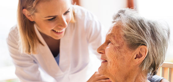 Female clinician, smiling down towards older female patient. 