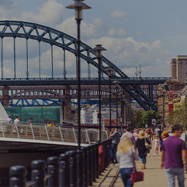 People walking alongside the Quayside with a view of the Tyne Bridge