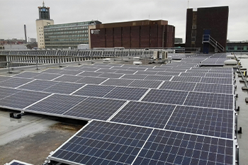 PV Arrays on the roof of a tall building, with more buildings in the distance. The sky is grey. 