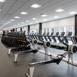 Gym with cardio equipment lined up against a glass wall.