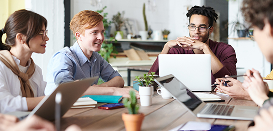 groupe of people sat around a desk infront of laptops