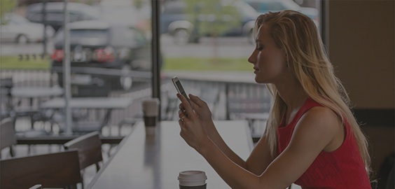 NU Connect: The Northumbria App page menu button - a woman browsing her mobile while sitting at a table with a cup of coffee.