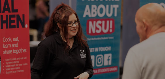 Image of a female member of Northumbria Students' Union staff manning a stand and talking to visitors