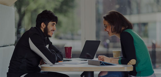 Image of a male student talking to a female member of staff across a table within Northumbria Student Central located in the university library