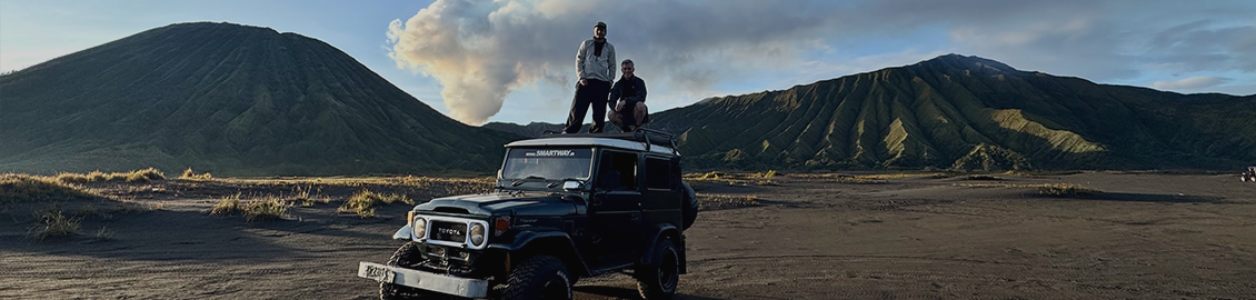 two people standing on a car with mountains in the background