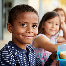 Young boy and girl at school lunch table smiling to camera
